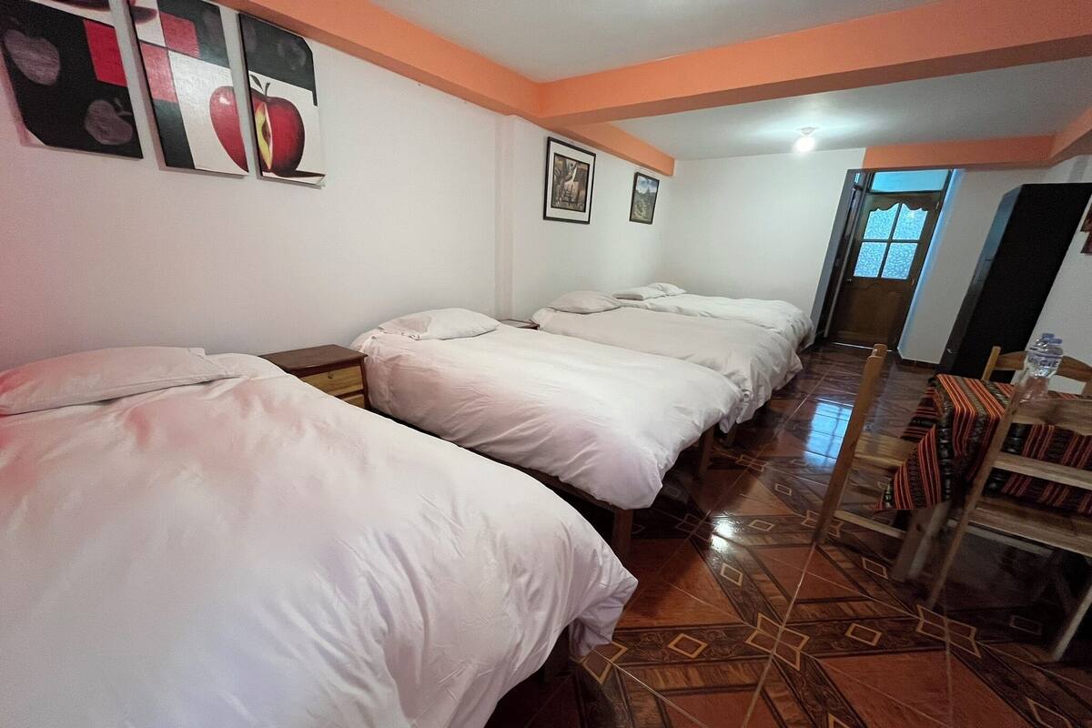 Ein Hotelzimmer mit vier nebeneinander stehenden Betten, einem Esstisch mit Stühlen und einem gemusterten Boden.