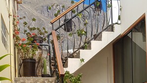 Una escalera con barandilla de metal que lleva a un segundo piso, rodeada de plantas en macetas y muebles de mimbre.