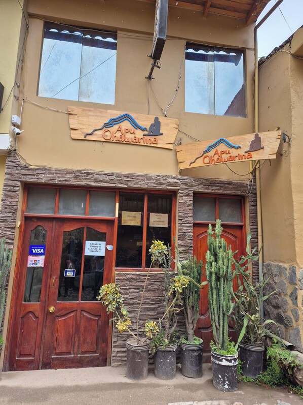 A two-story building with a wooden sign reading "Apu Ohawarina" and a wooden door with a "VISA" sign. - Hostal Apu Qhawarina (Ollantaytambo)