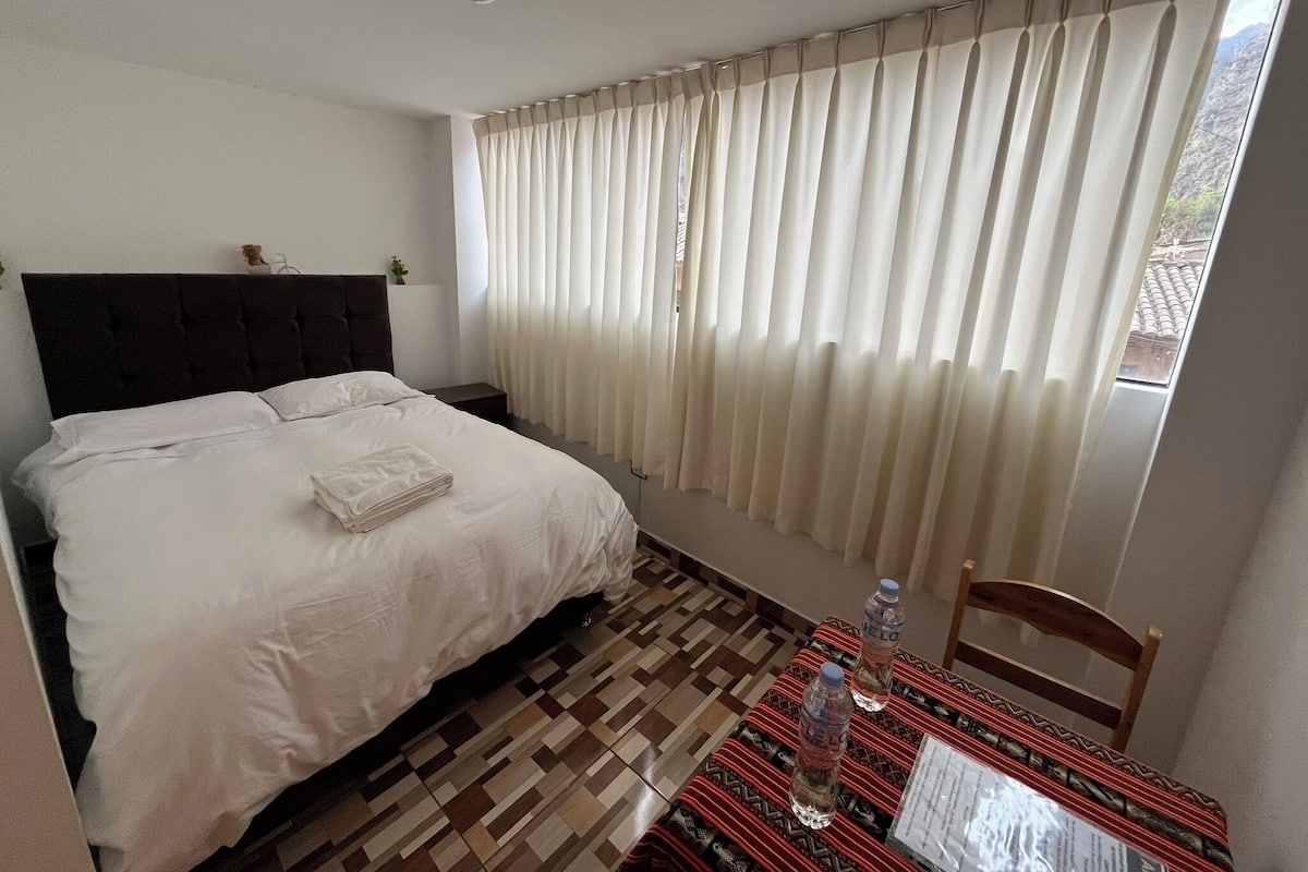 Ein Hotelzimmer mit einem Bett, einem Tisch mit Wasserflaschen und einem Stuhl.
