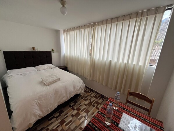 A hotel room with a bed, a table with water bottles, and a chair.