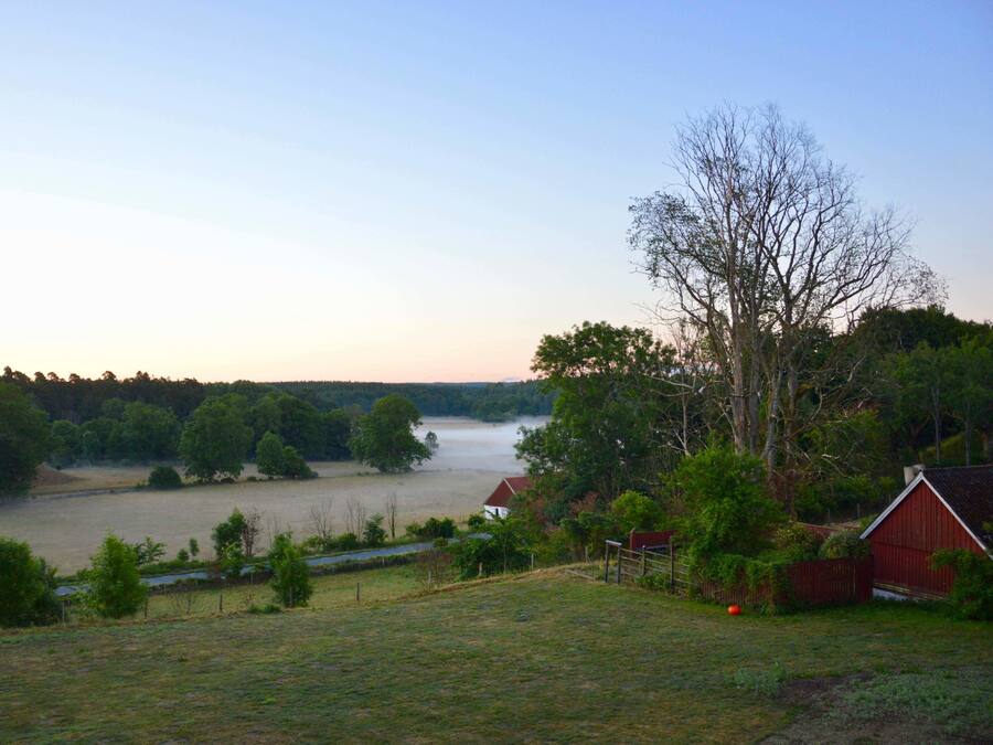 A rural landscape with a river, trees, and a red barn.