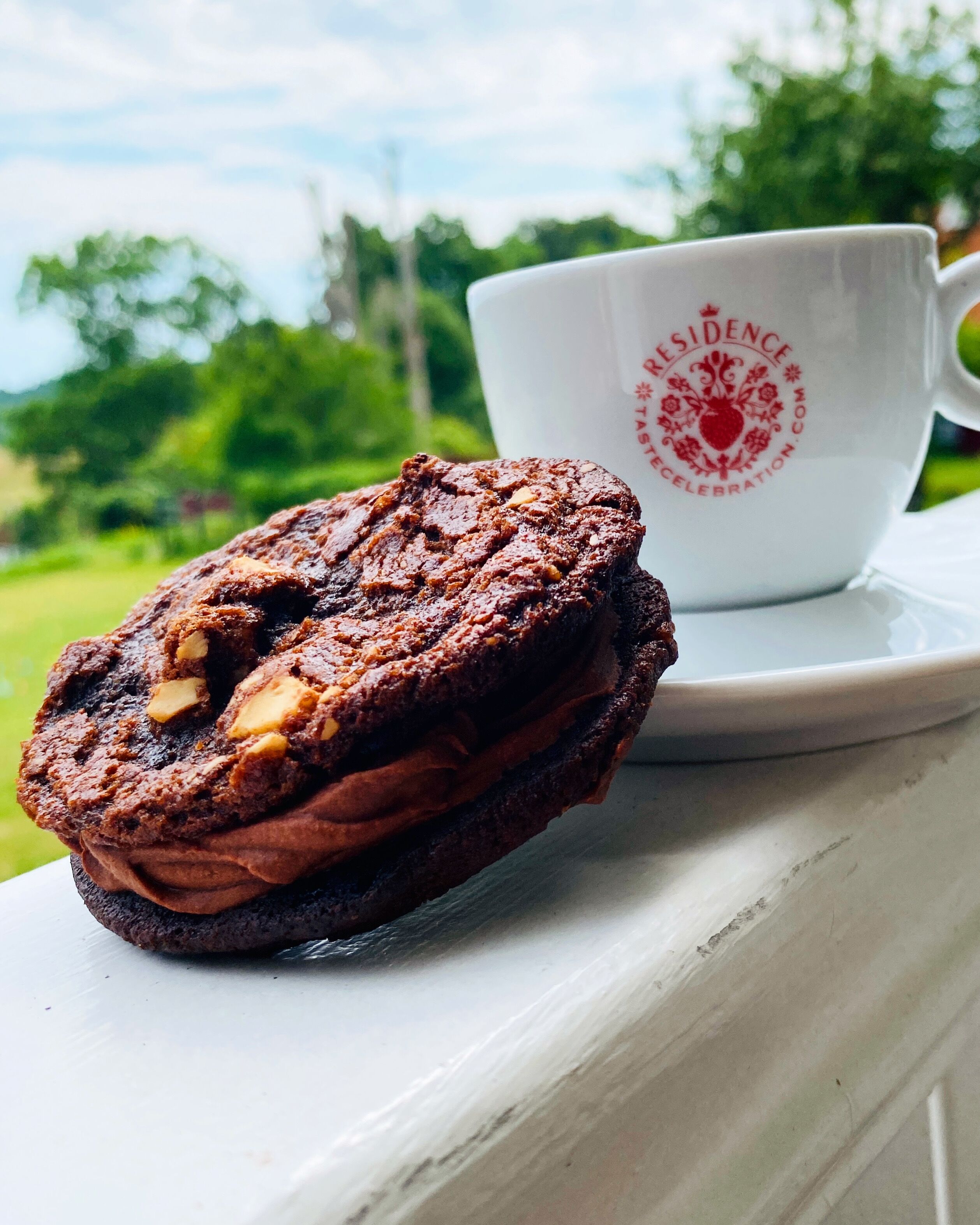 Un muffin de chocolate con un nuez visible sobre un plato blanco, junto a una taza blanca con texto rojo.