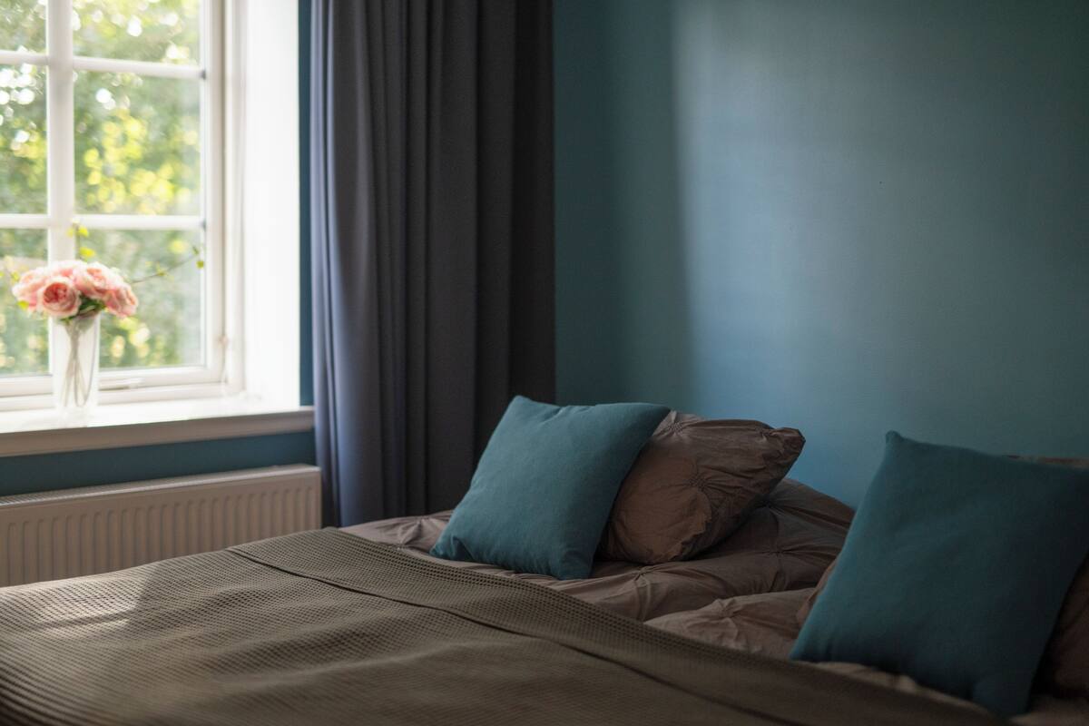 A bedroom with a bed, a window with curtains, and a vase with flowers.