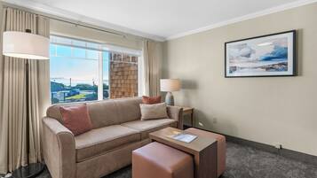 A hotel room with a beige sofa, a small ottoman, a lamp, and a framed picture on the wall.