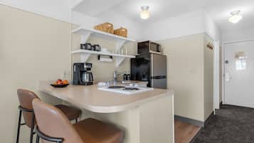 A compact kitchen with a central island, bar stools, a microwave, a refrigerator, and a coffee maker.