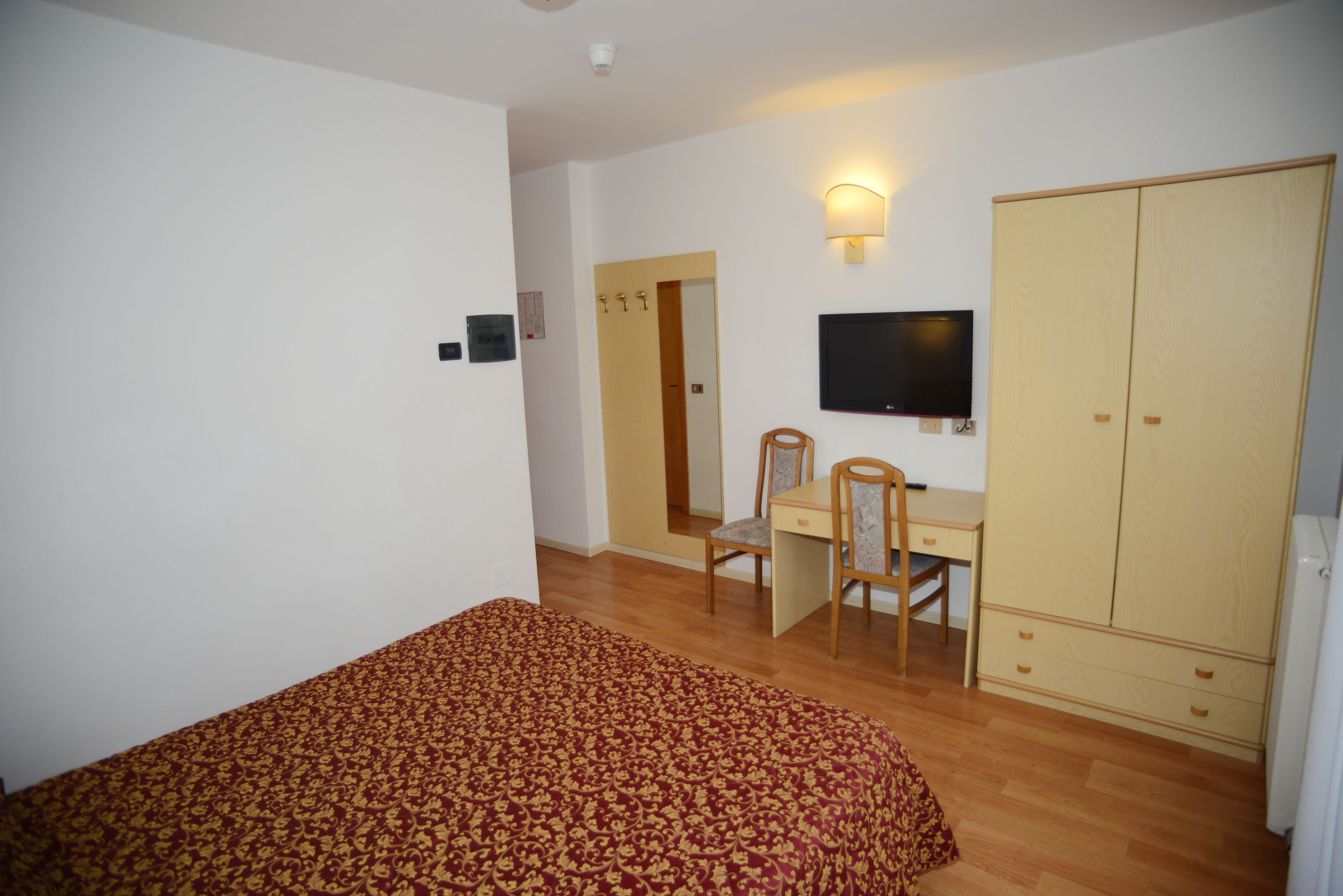 A bedroom with a bed, a desk with a chair, a television, and a wardrobe.