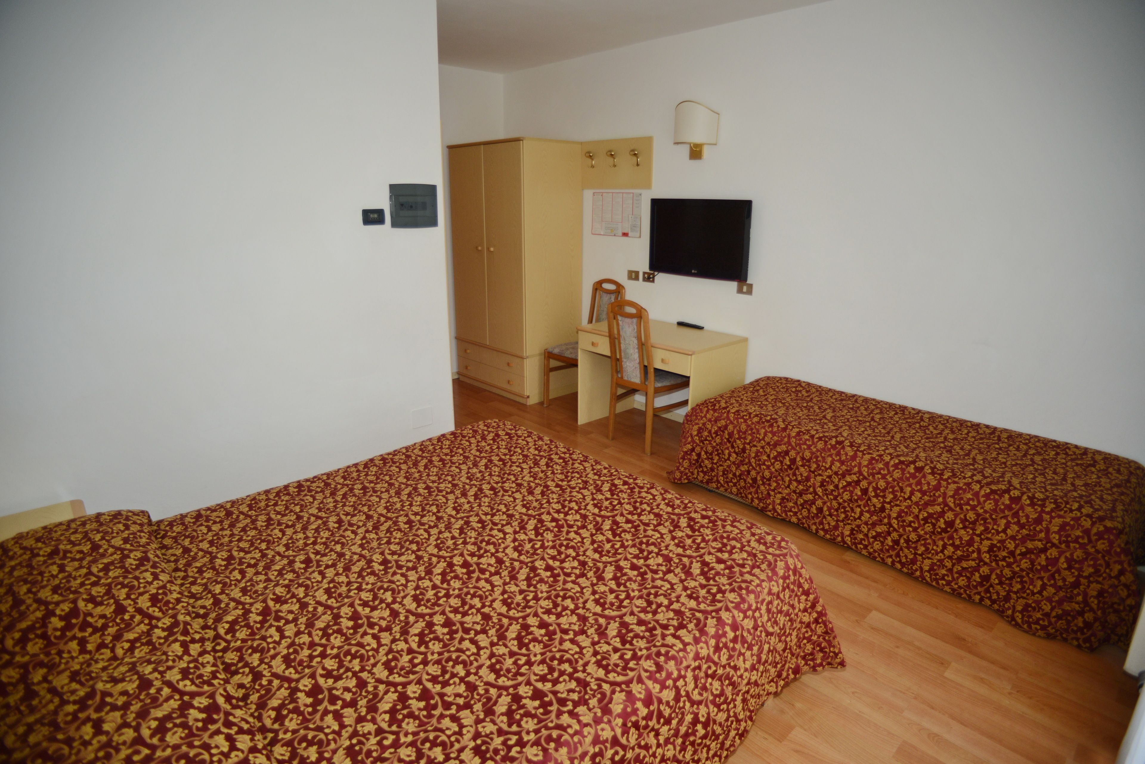 A bedroom with two single beds, a desk with a chair, a wardrobe, and a television.