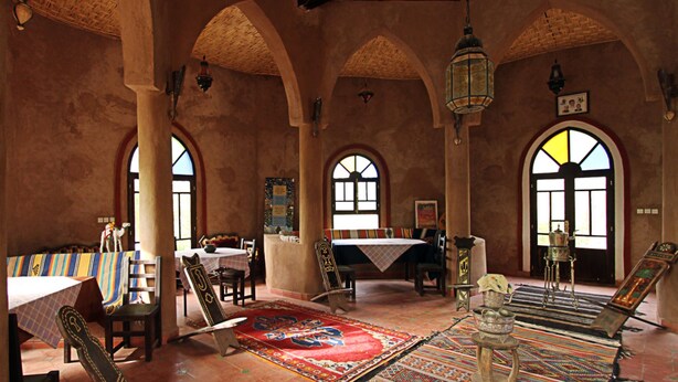 A traditional interior with high arched ceilings, patterned rugs, and a central table. - Jnane dar diafa (Tamegroute)