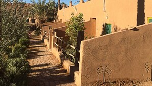 A pathway leading to a building with a traditional architectural style, surrounded by palm trees and a clear blue sky. - Jnane dar diafa (Tamegroute)