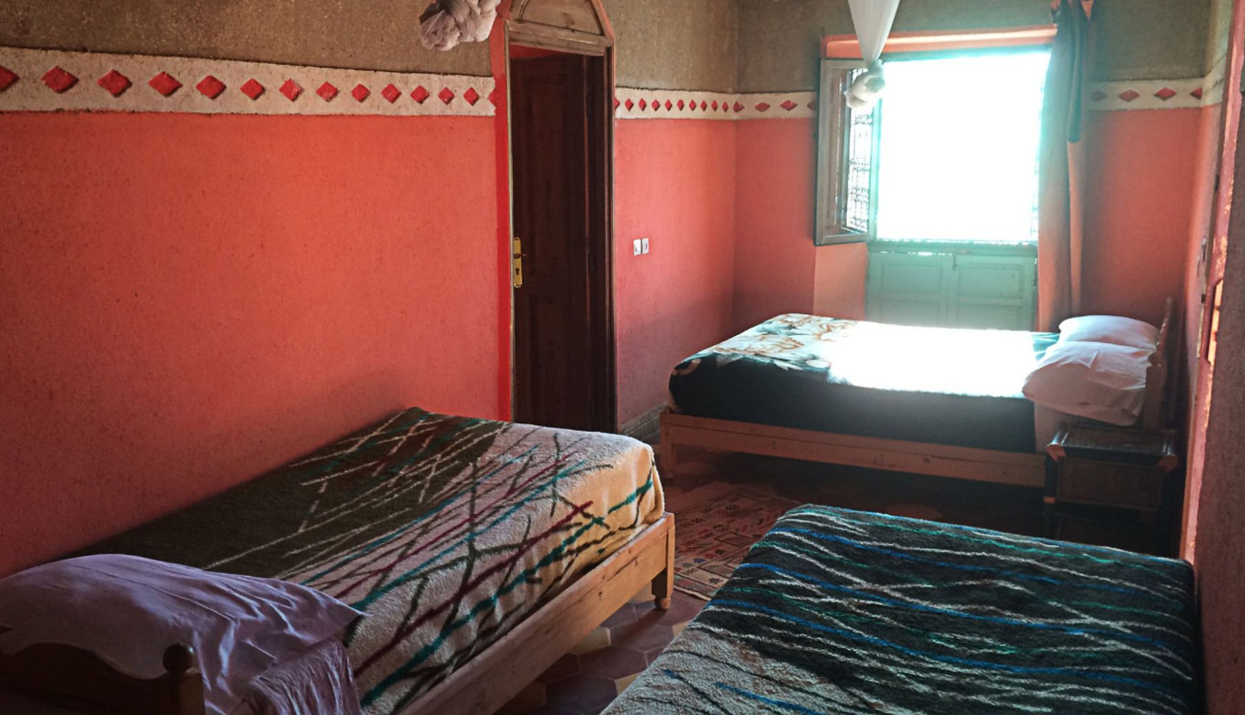 Een kamer met twee éénpersoonsbedden, een houten deur en een raam met gordijnen.