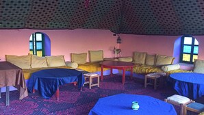 A cozy room with a patterned ceiling, a sofa set, a round table, and a small chair. - Jnane dar diafa (Tamegroute)