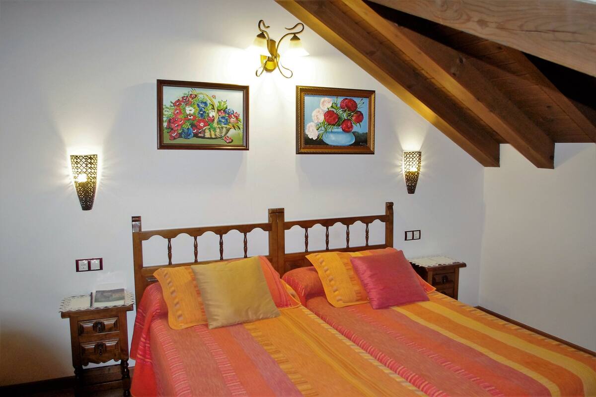 Une chambre à coucher avec un lit en bois, deux lampes fixées au mur et deux tableaux représentant des motifs floraux, encadrés.