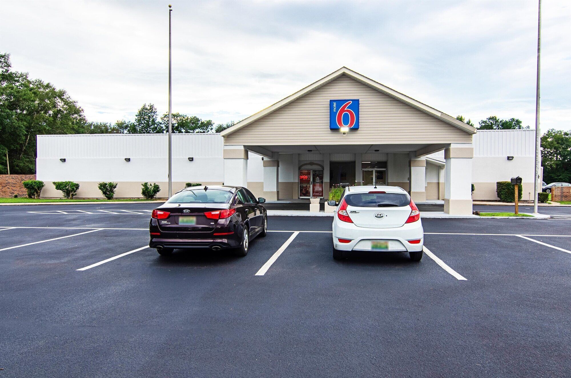 A motel with a large sign indicating it is number 6. There are two cars parked in the parking lot.