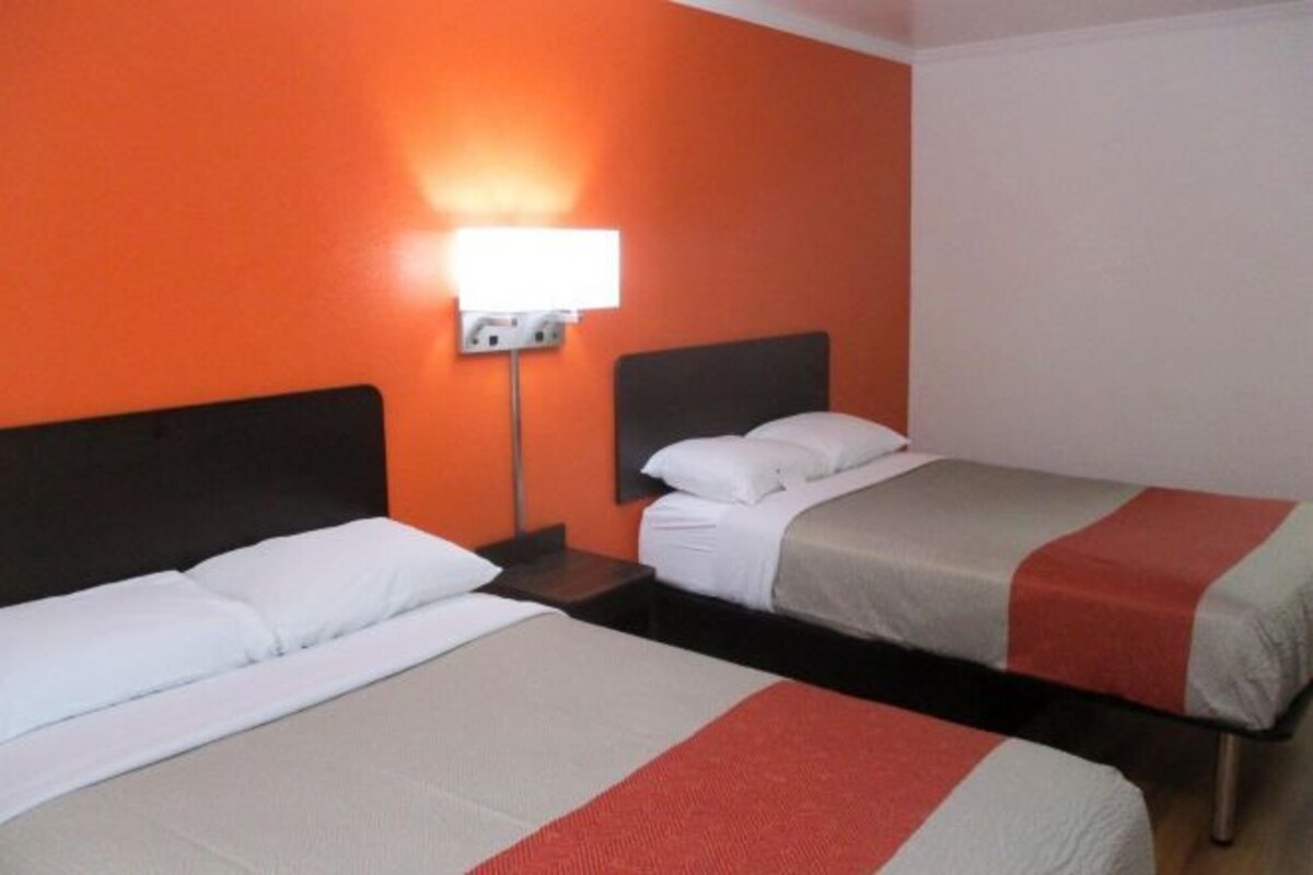Deux lits avec une literie blanche et rouge, une table de chevet avec une lampe et un mur orange.
