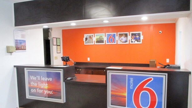 A motel reception desk with a large sign reading "motel 6" and a sign on the left stating "We'll leave the light on for you." - Motel 6 Bay Minette, AL (Bay Minette)