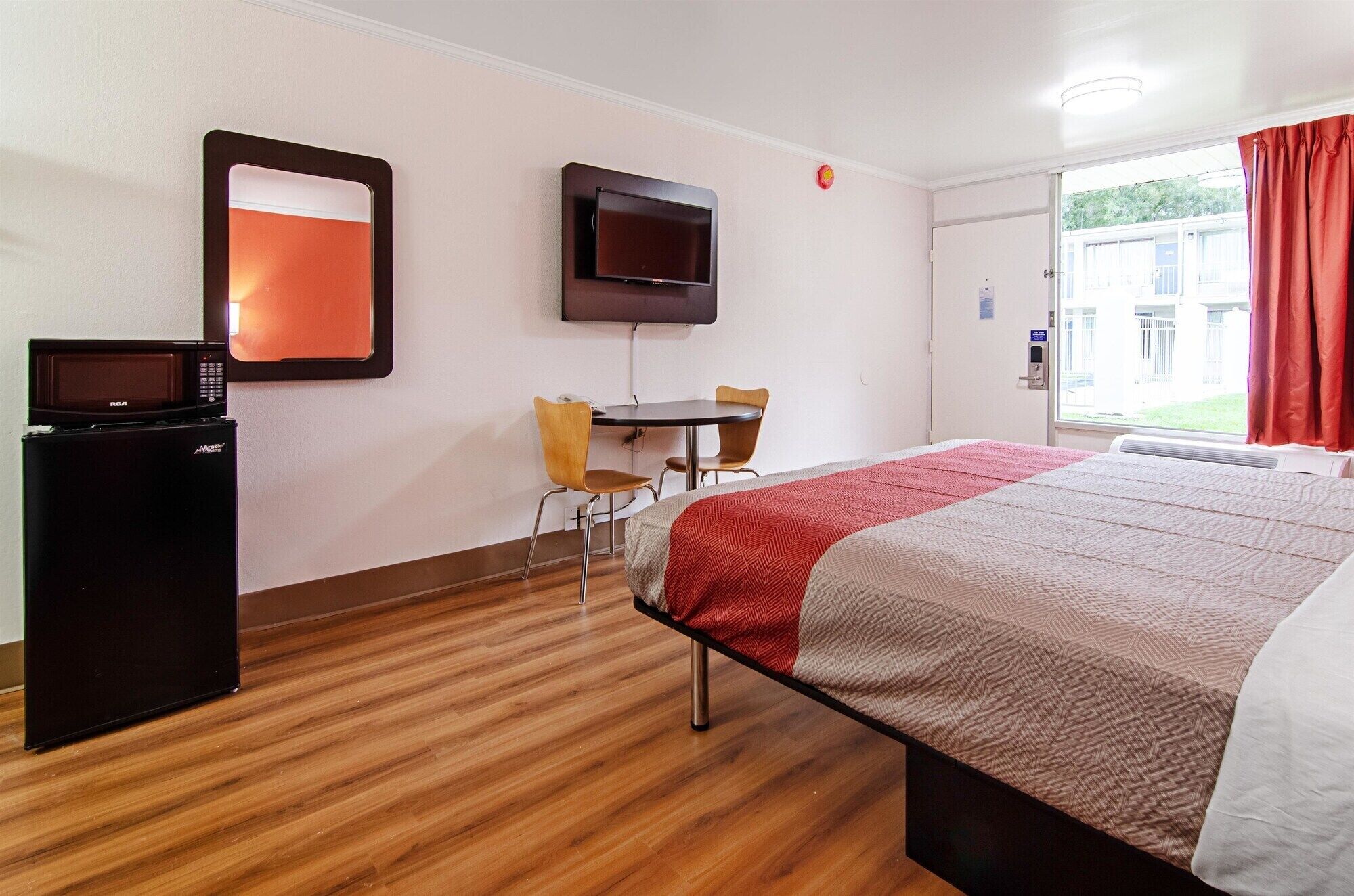 A hotel room with a bed, a desk with two chairs, a television mounted on the wall, and a microwave on a small cabinet.