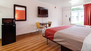 A hotel room with a bed, a desk with two chairs, a television mounted on the wall, and a microwave on a small cabinet.