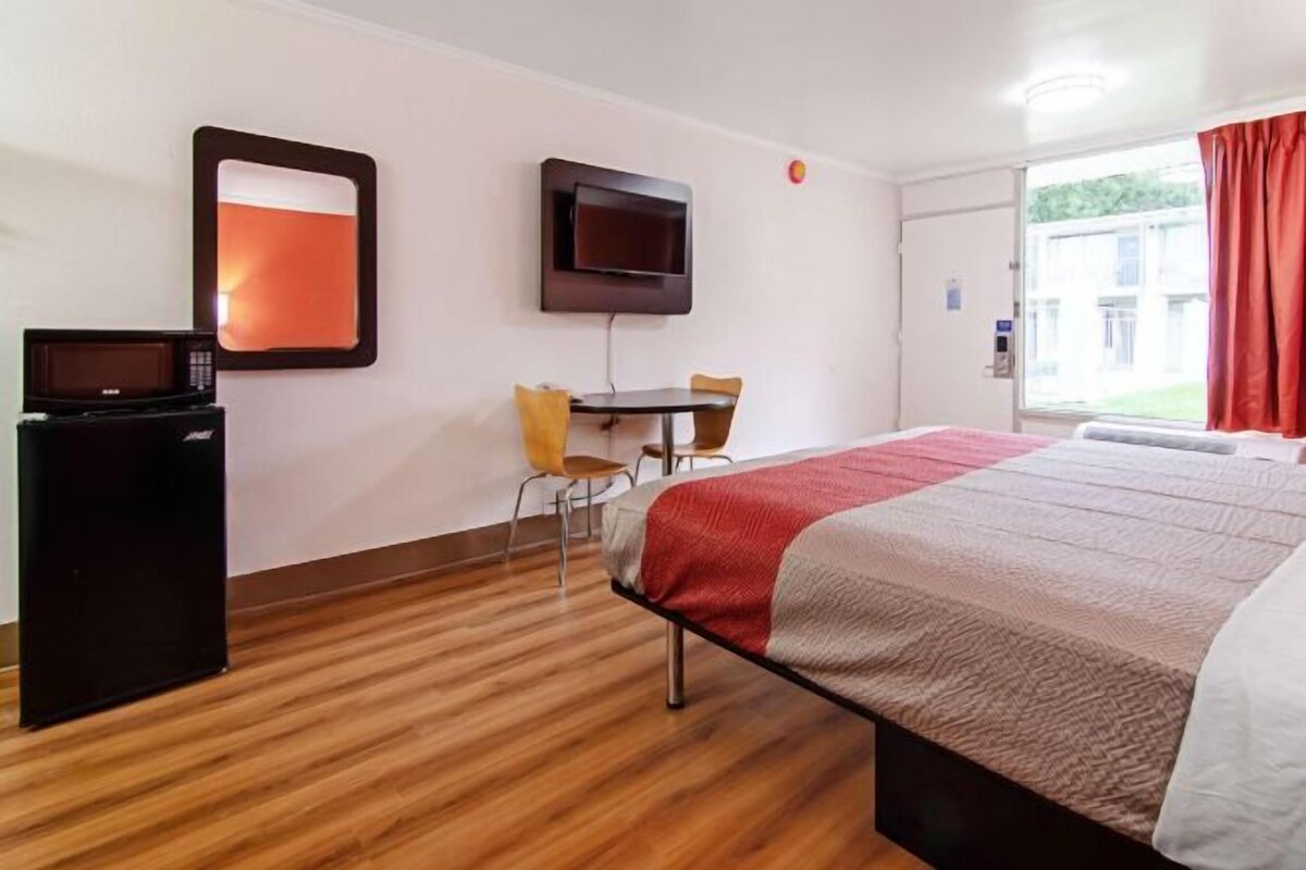 Une chambre d’hôtel équipée d’un lit, d’un bureau, d’une chaise, d’une télévision et d’une fenêtre avec des rideaux.