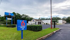A motel sign with a '6' and 'ENTER' arrow, a parking lot, and a building with a '6' logo. - Motel 6 Bay Minette, AL (Bay Minette)