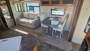 Interior compacto de uma motorhome, com sofá, mesa de jantar e cadeiras.