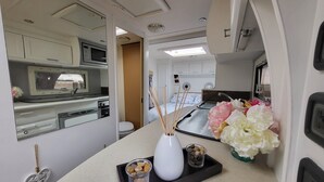 Uma kitchenette compacta com micro-ondas, pia e armários. Há uma pequena mesa com um vaso e objetos decorativos.