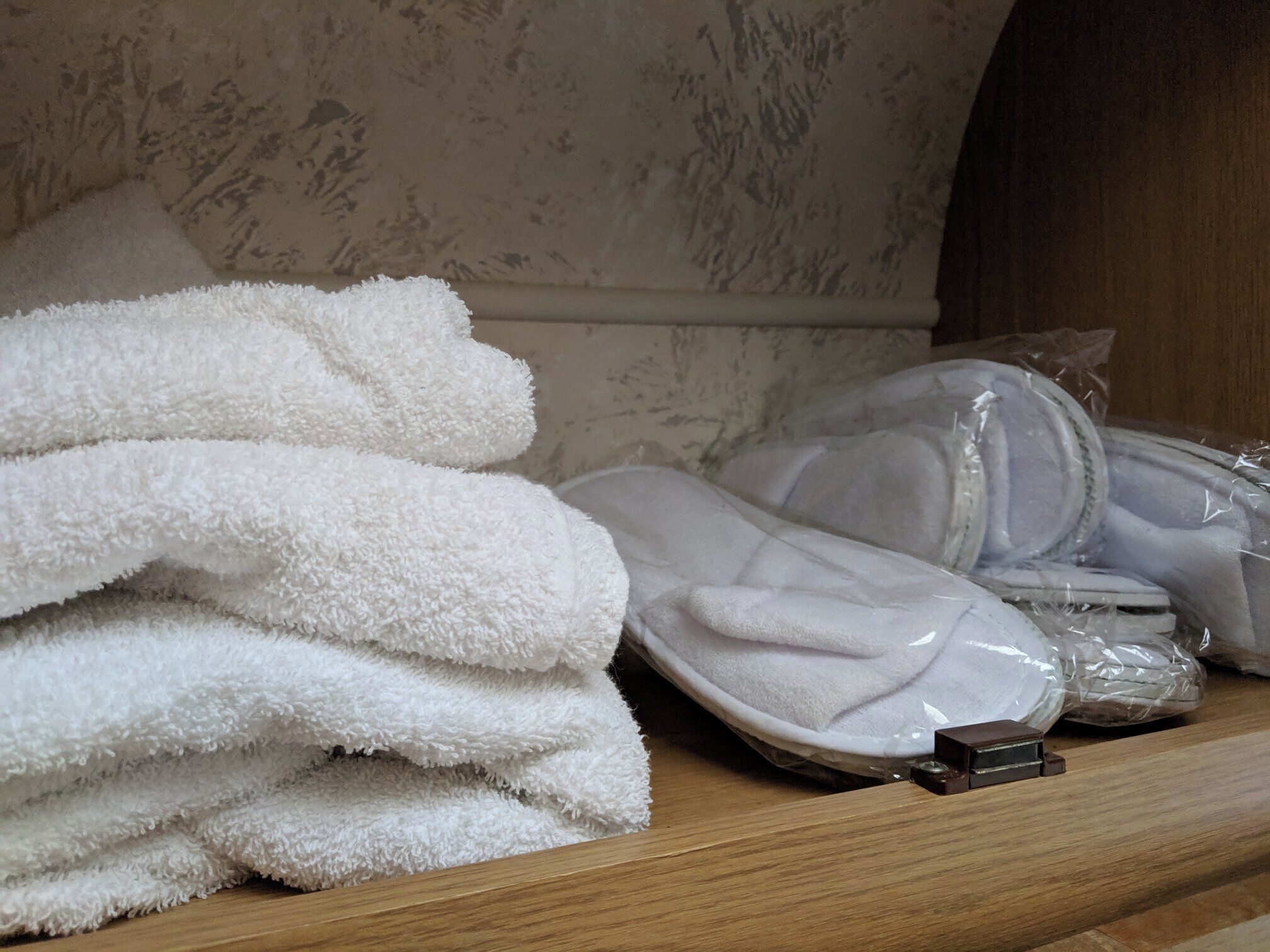 A stack of white towels and a plastic bag with a white item on a wooden surface.