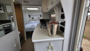 Interior compacto de RV com cozinha compacta, uma cama com roupa de cama florida e uma janela pequena.