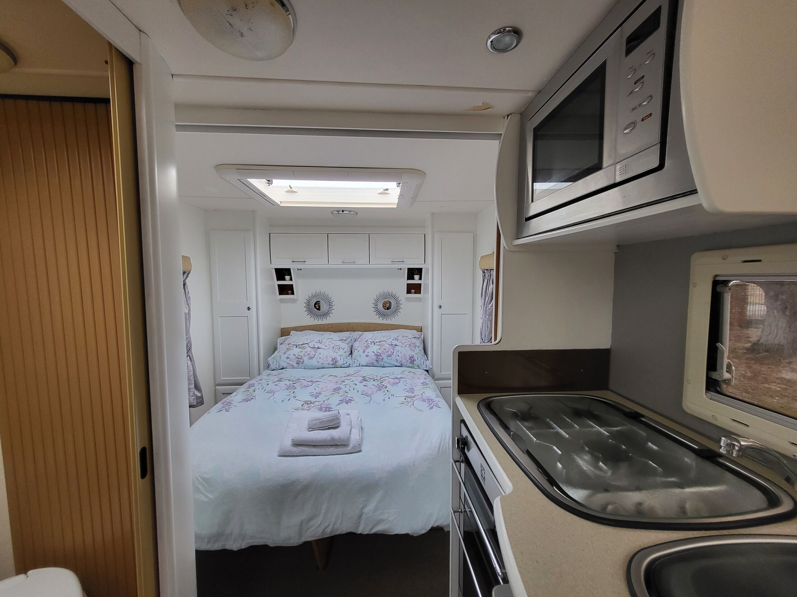 Ein kompaktes Wohnmobil-Interieur mit Bett, Küchenzeile und kleinem Badezimmer.