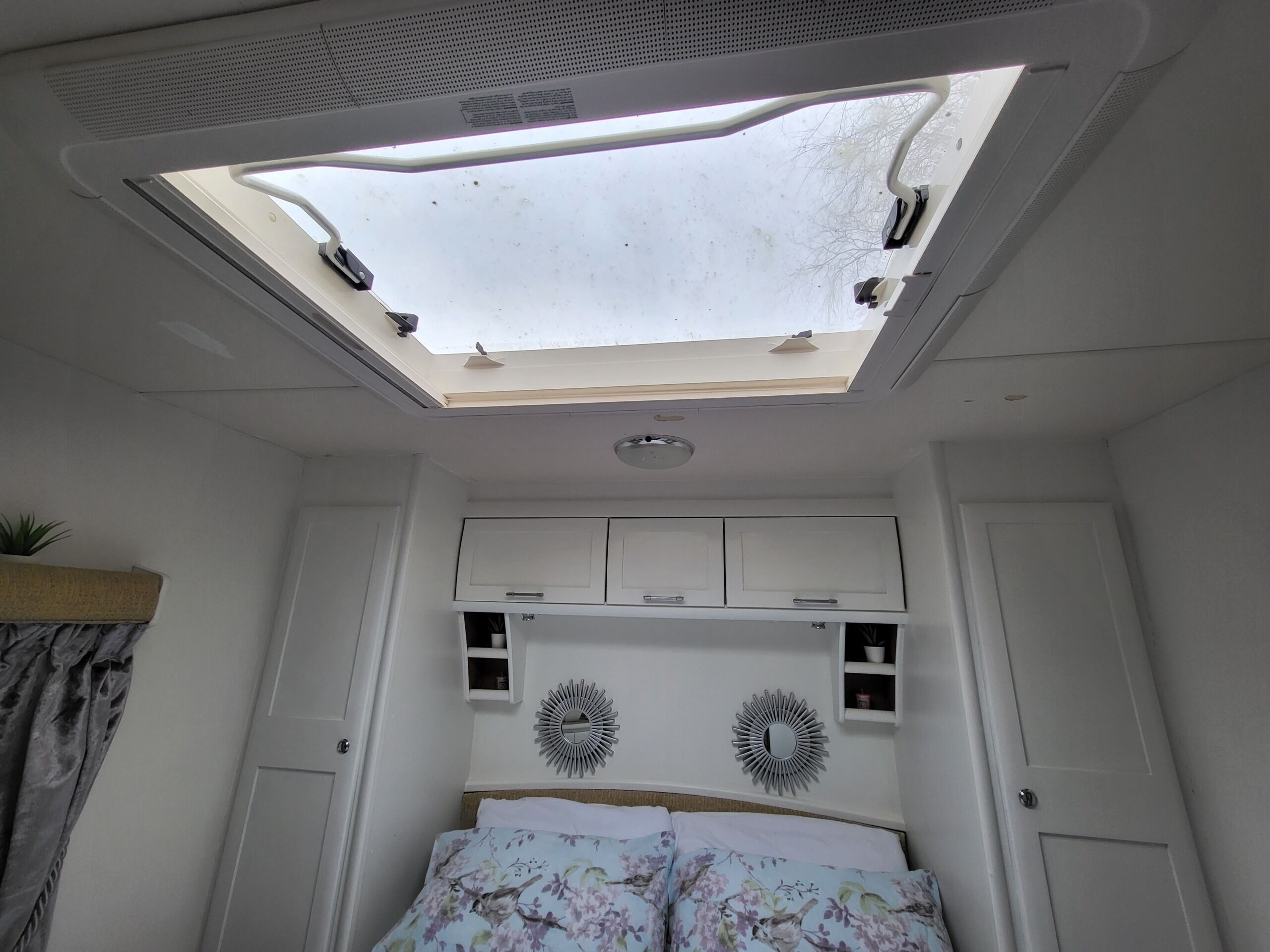 A bedroom with a skylight, a bed with floral bedding, and a white wardrobe.