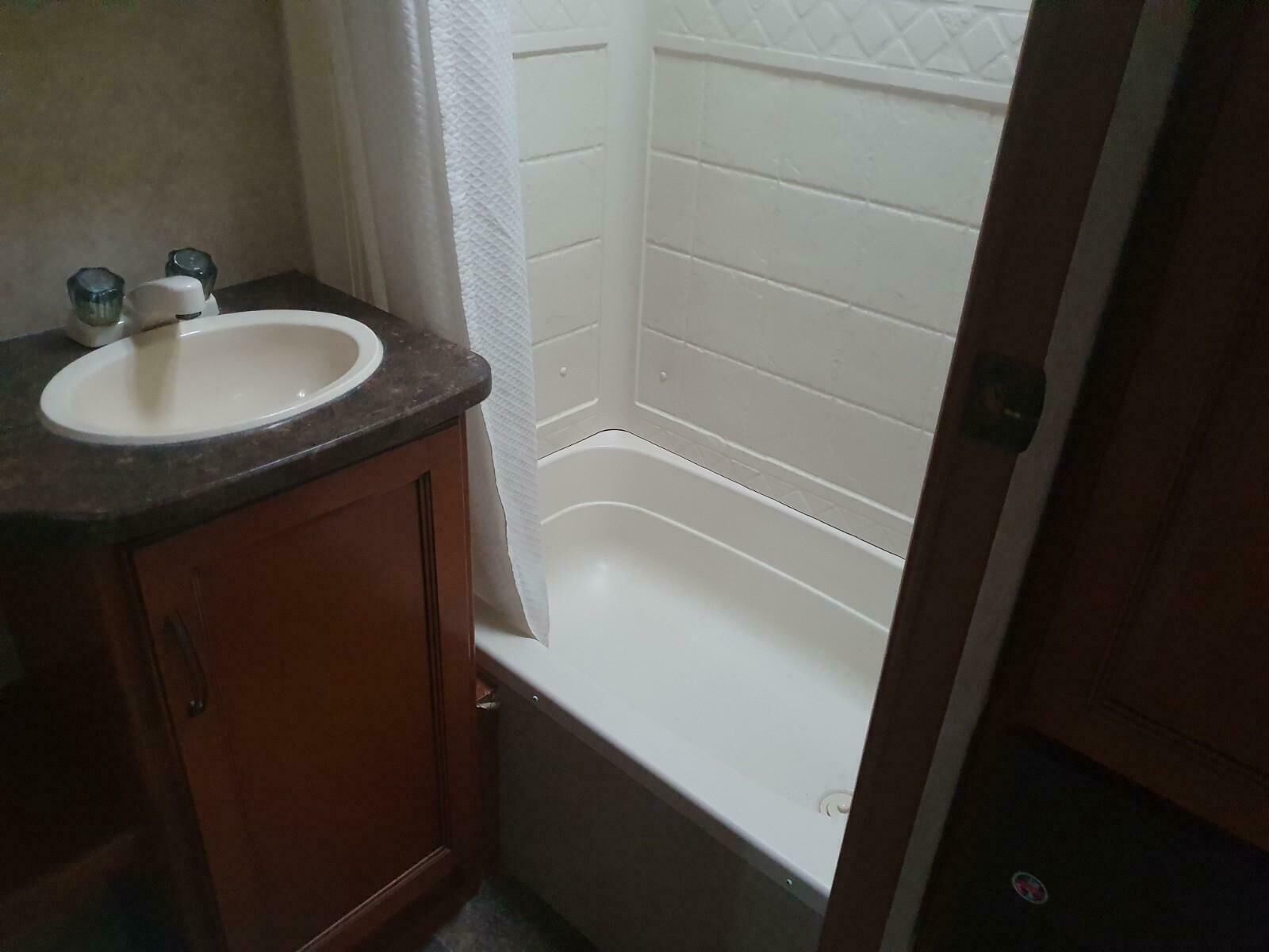 A bathroom with a white sink, wooden cabinet, and a white bathtub.