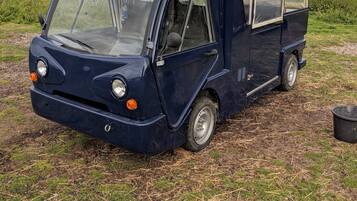 Un piccolo veicolo blu scuro parcheggiato in un campo sotto un cielo sereno.