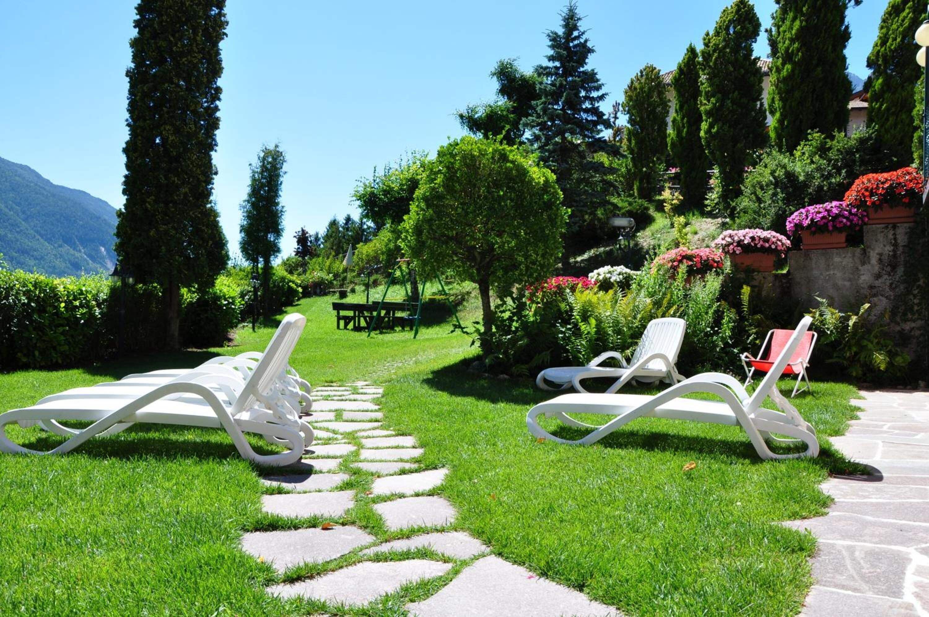 Een tuin met een pad van stenen, witte lounge fauteuils en een picknicktafel.