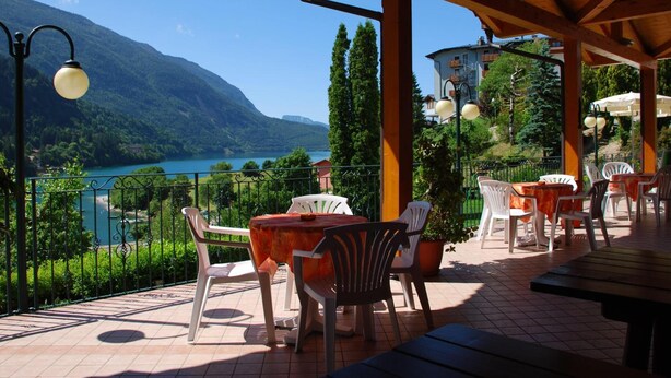 Una terraza al aire libre con mesas y sillas, con vistas a un lago y montañas.