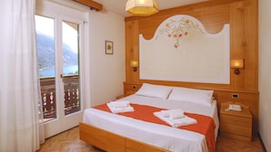 Habitación de hotel con cama de madera, un ventanal con vistas a montañas, una araña y una mesita de noche con lámpara.