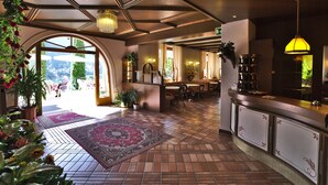 Un vestíbulo amplio con piso a cuadros, un mostrador de recepción y un gran arco que da al exterior.