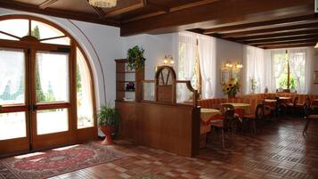 Ein traditionelles Gasthaus mit Holzmöbeln, einer zentralen Rezeption und einem Essbereich mit Tischen und Stühlen.