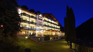 Un hotel de varios pisos con fachada iluminada, múltiples balcones y un jardín delantero ajardinado.