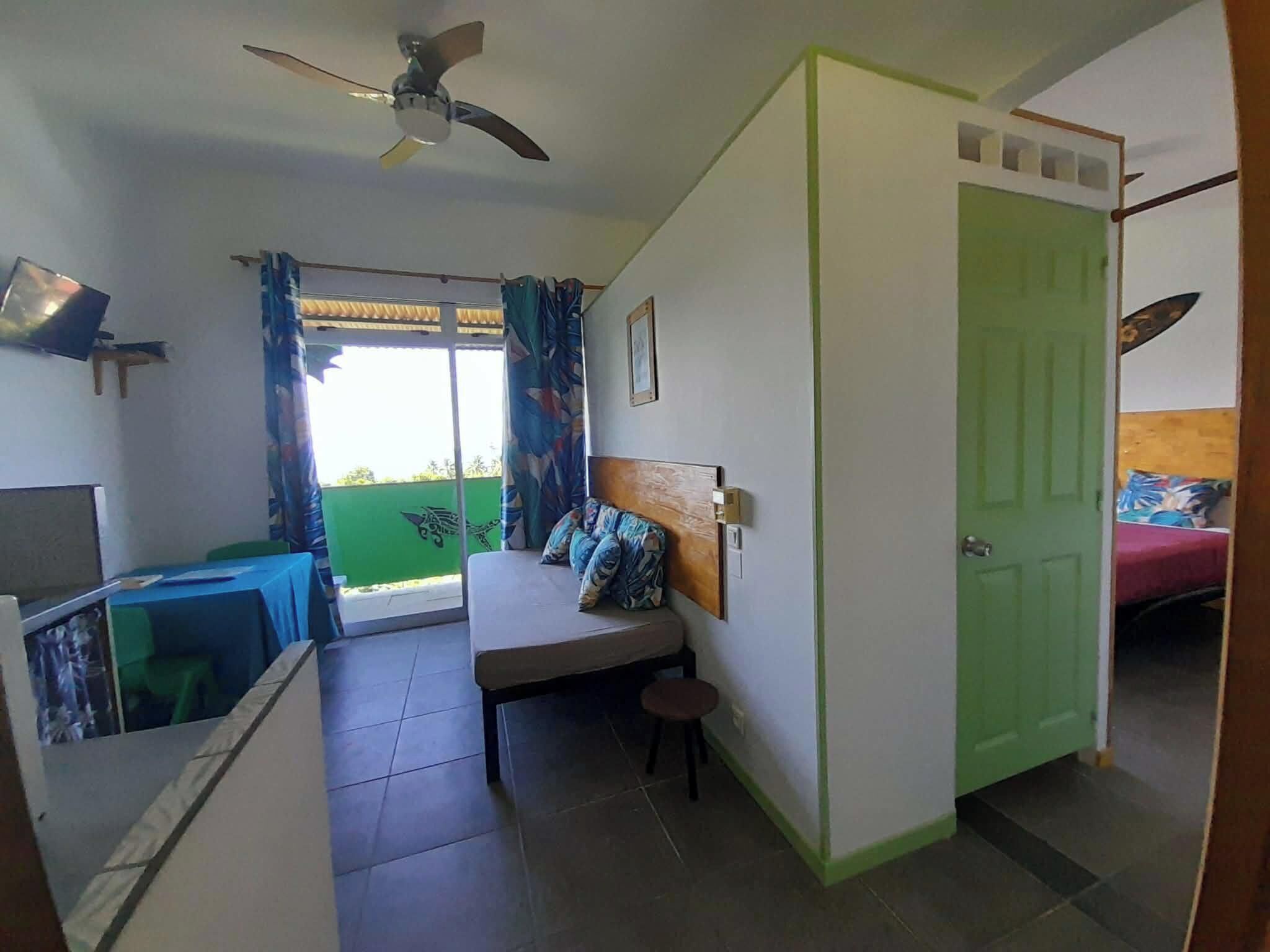 A room with a bed, a desk, a chair, a ceiling fan, and a green door.
