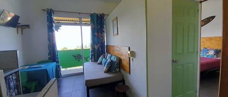 A room with a bed, a desk, a chair, a ceiling fan, and a green door.