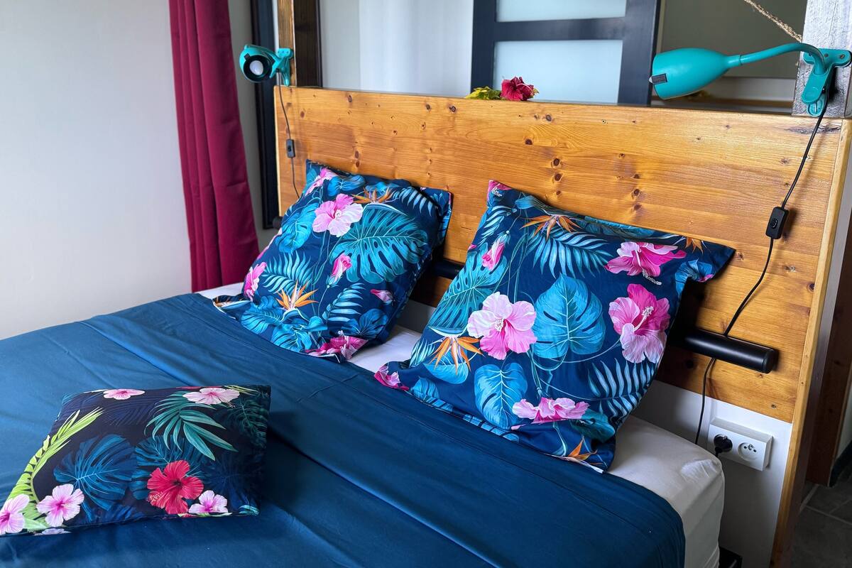 A bed with a wooden headboard, two floral-patterned pillows, and a blue bedspread.