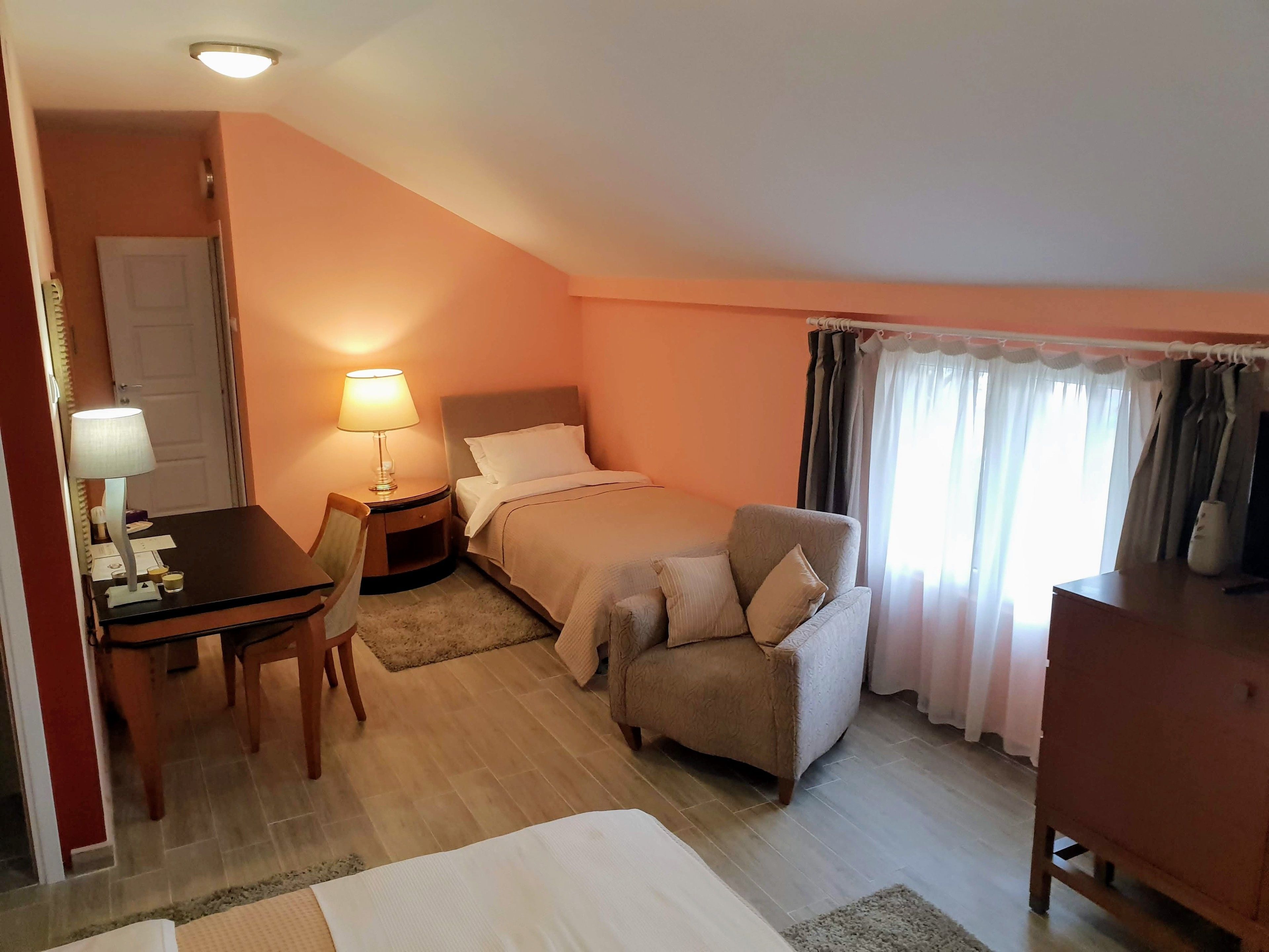 Hotellihuone, jossa on sänky, kirjoituspöytä lampun kanssa, tuoli, sohva ja lipasto.
