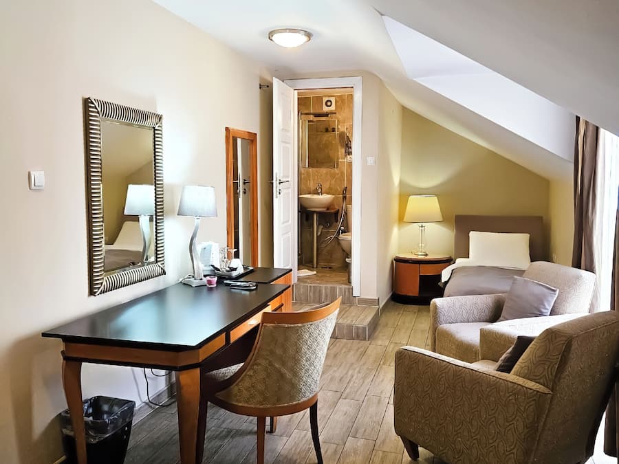 Una habitación de hotel con escritorio, dos sillas, cama, baño y una escalera.