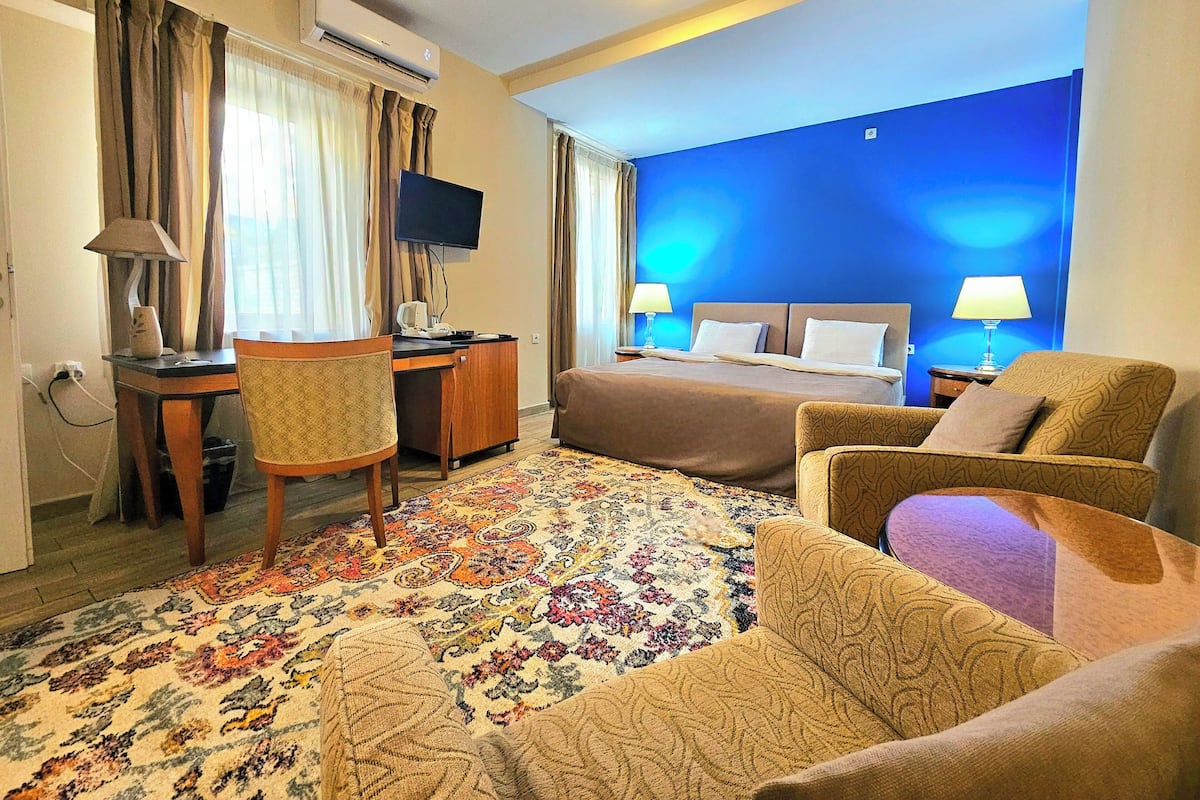 Ein Hotelzimmer mit einem Bett, zwei Stühlen, einem Schreibtisch, einem Fernseher und einer Klimaanlage.