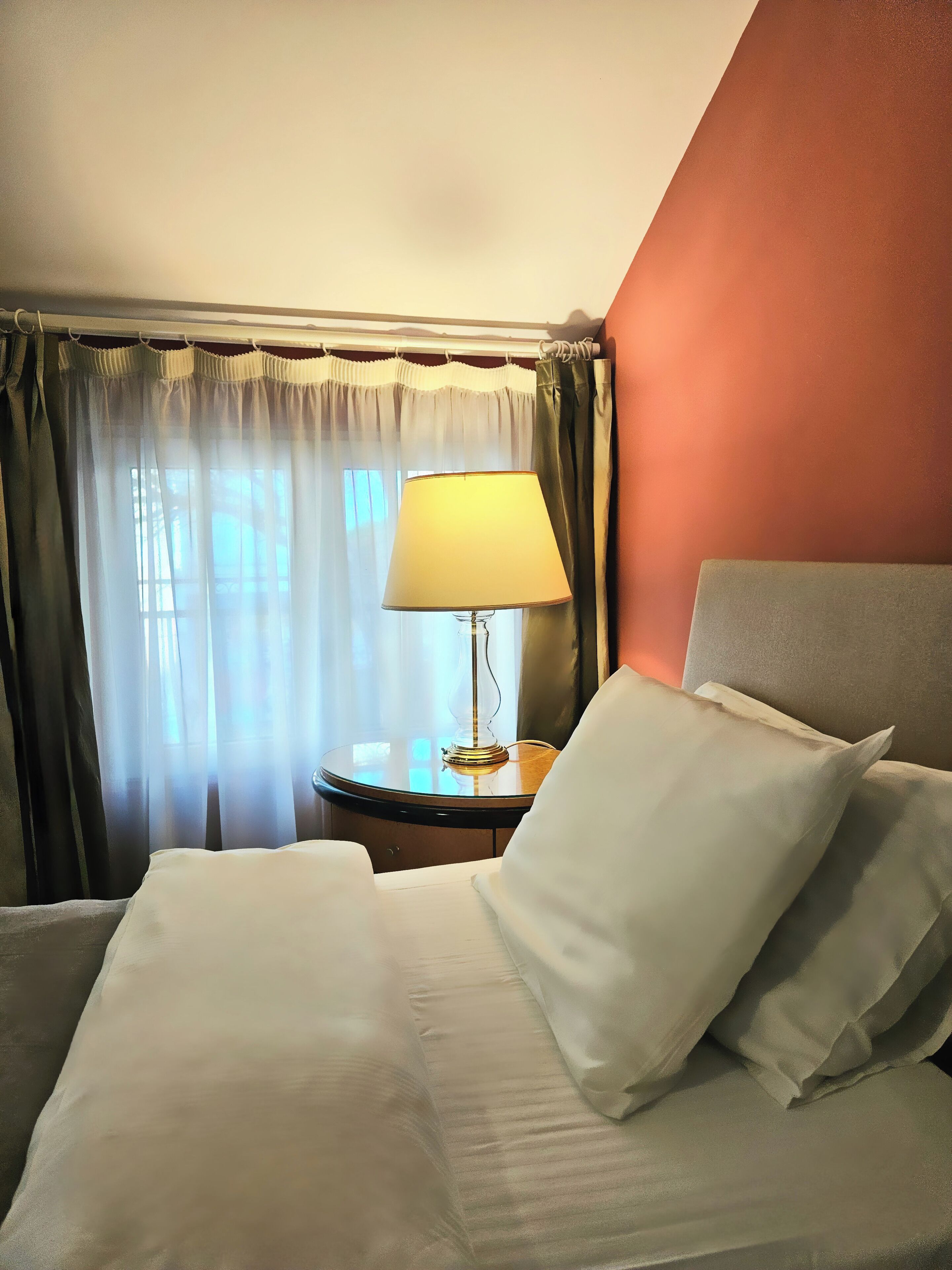 A hotel room with a bed, a nightstand with a lamp, and a window with curtains.