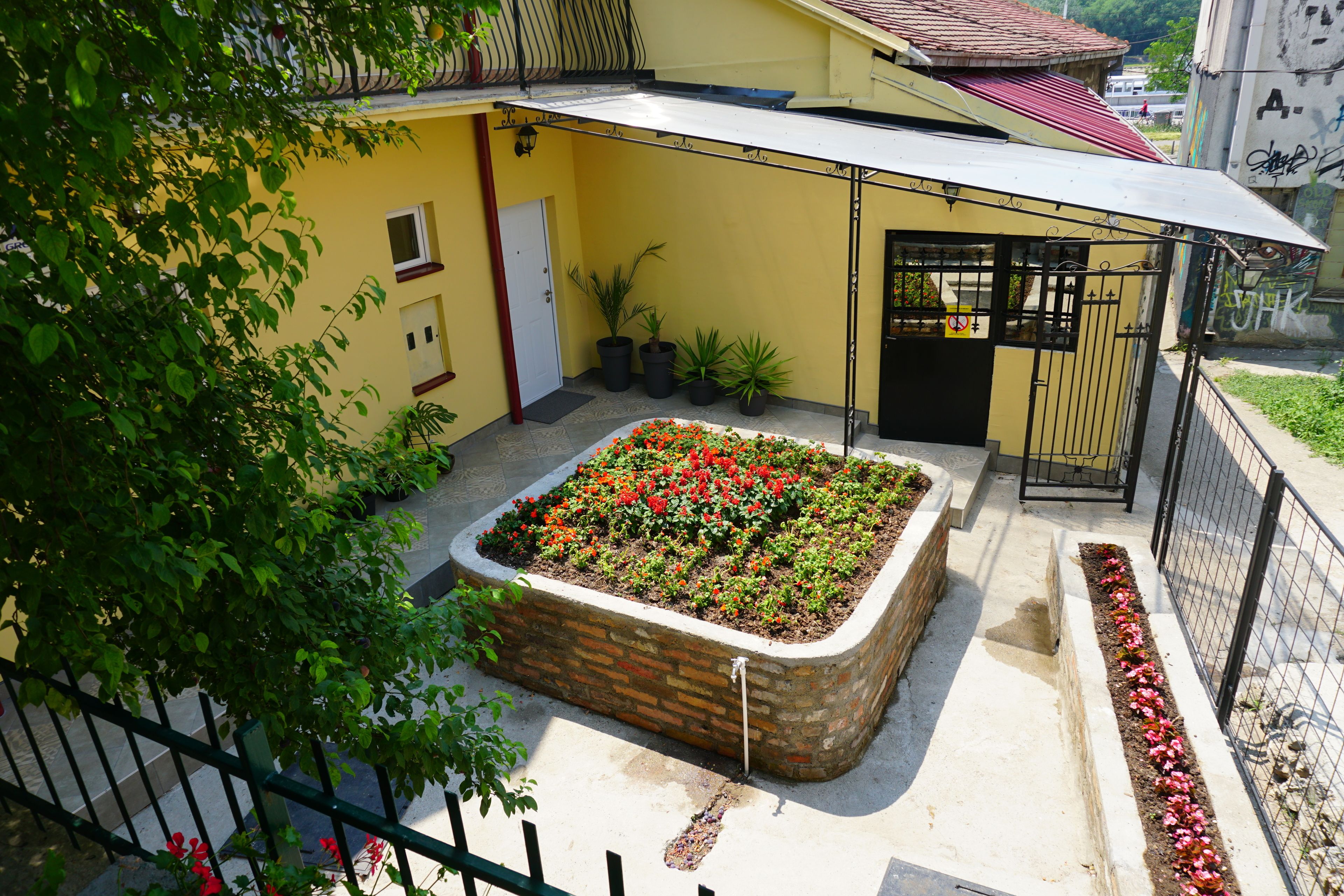 A courtyard with a flower bed, a covered area, and a gated entrance.