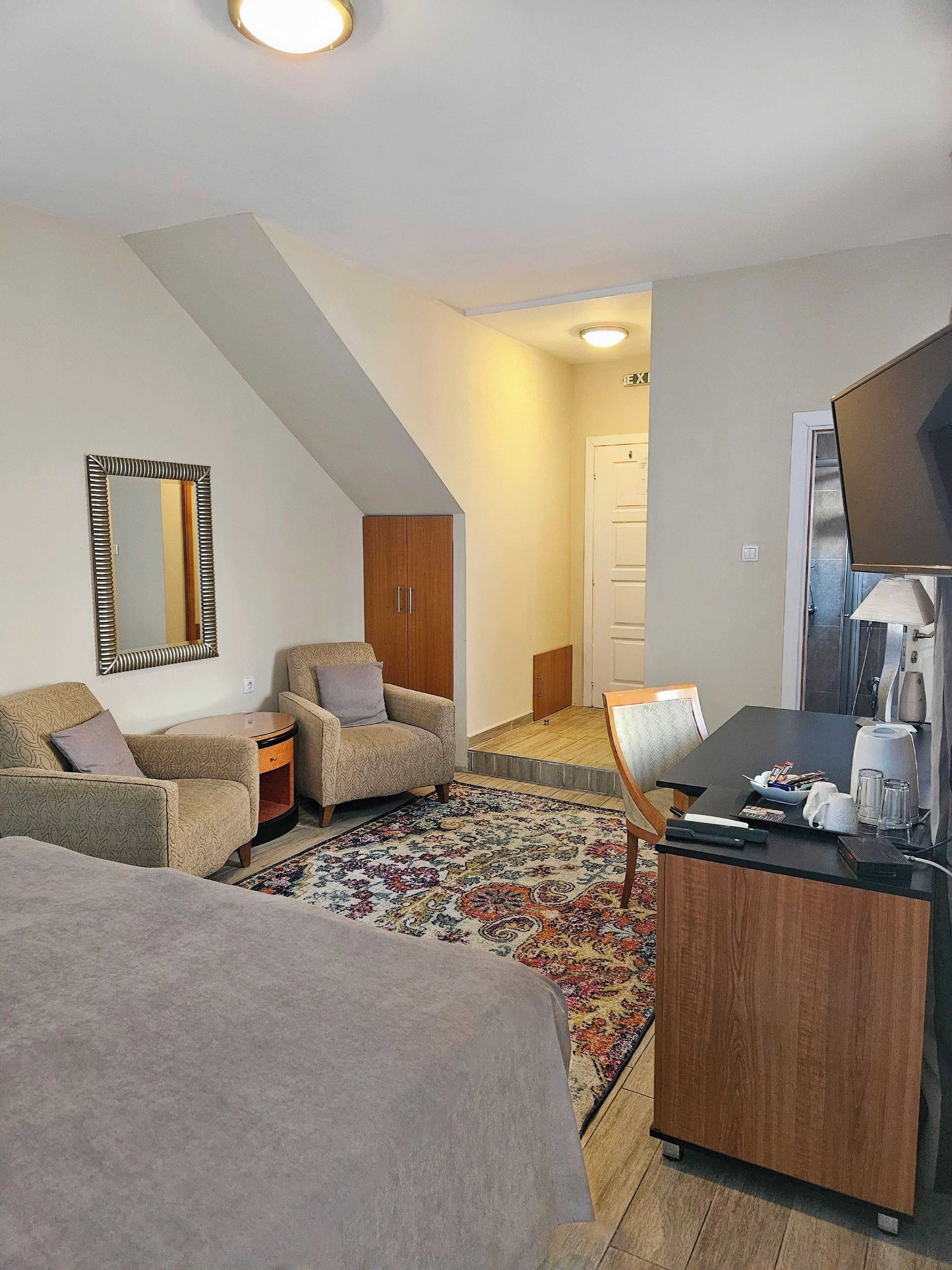 A hotel room with a bed, two armchairs, a small table with a lamp, a TV, and a wardrobe.