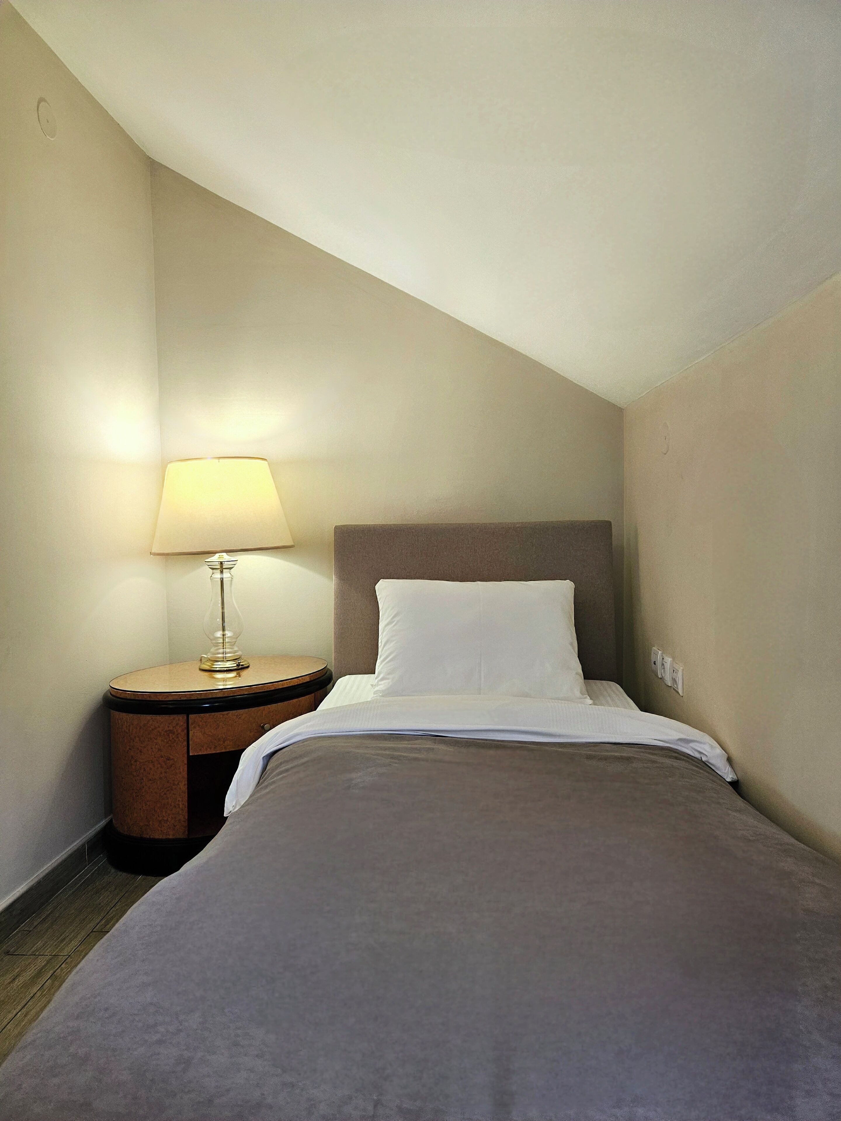 Une chambre d’hôtel avec un lit simple, une table de chevet avec une lampe et un plancher en bois.