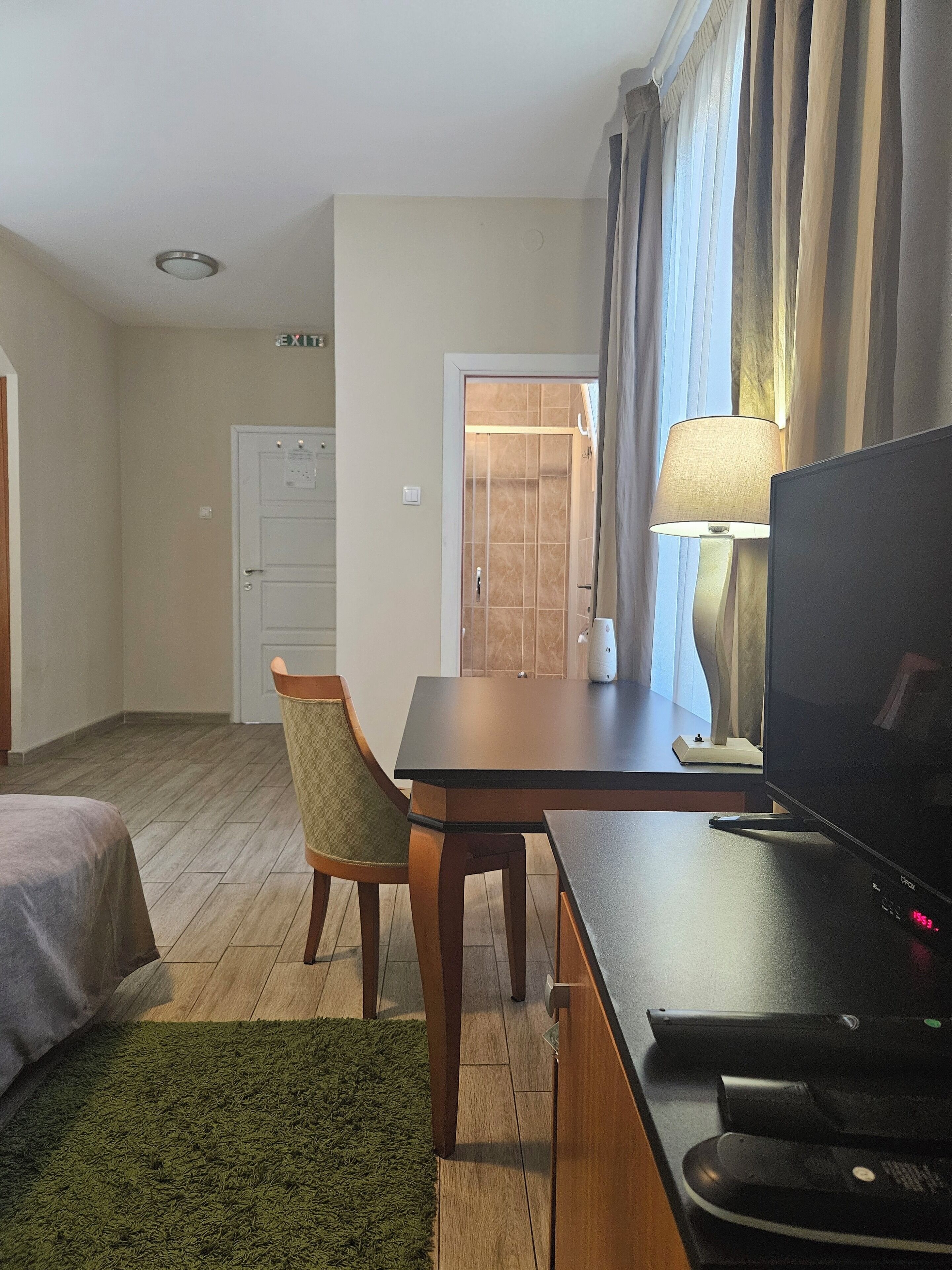 Ein Hotelzimmer mit einem Bett, einem Schreibtisch mit Fernseher, einem Sessel, einer Lampe und einer Tür zu einem Badezimmer.