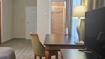Ein Hotelzimmer mit einem Bett, einem Schreibtisch mit Fernseher, einem Sessel, einer Lampe und einer Tür zu einem Badezimmer.